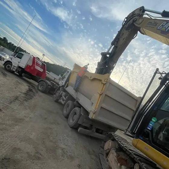 Escavadeira e caçamba sendo removidas de canteiro de obra